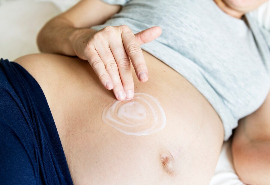 pregnant-woman-applying-body-cream-baby-bump_53876-14755
